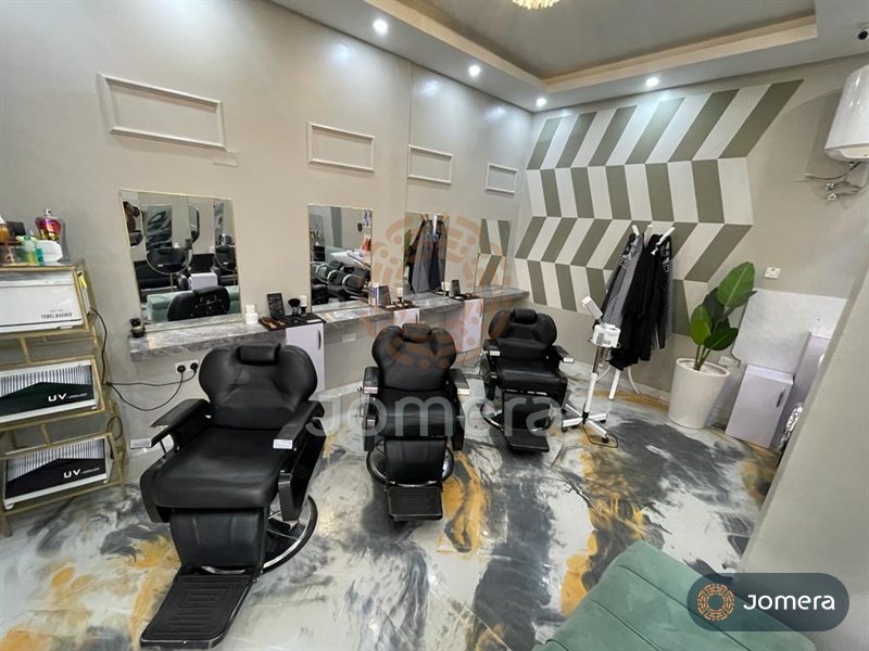 Barber stations with marble-look counters, brass-framed mirrors, a sage-and-white chevron feature wall and a marbled epoxy floor