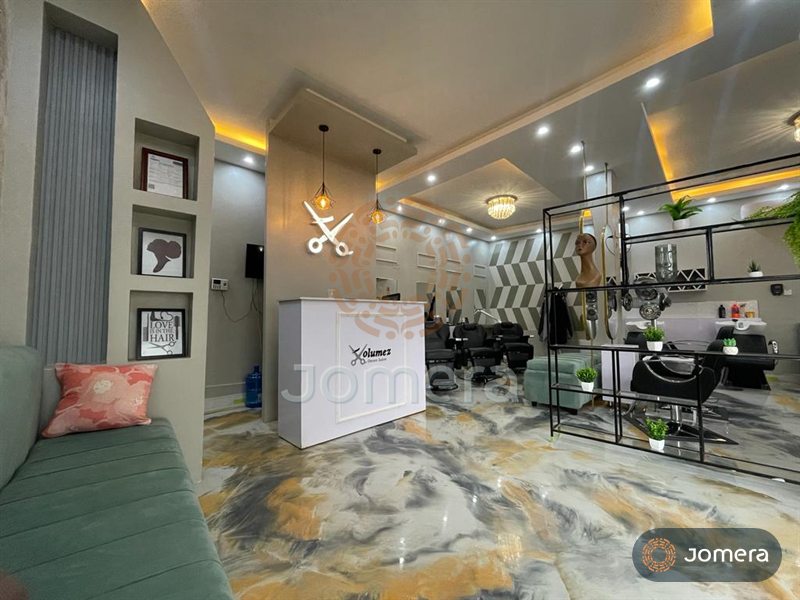 Salon reception with a white panelled desk under wire pendants, display niches, a sage velvet banquette and a marbled epoxy floor