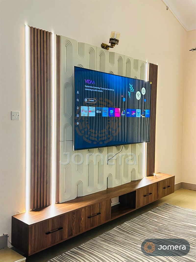 Side view of a custom TV wall with sculpted relief panels, lit fluted timber columns and a long floating walnut unit with black bar handles